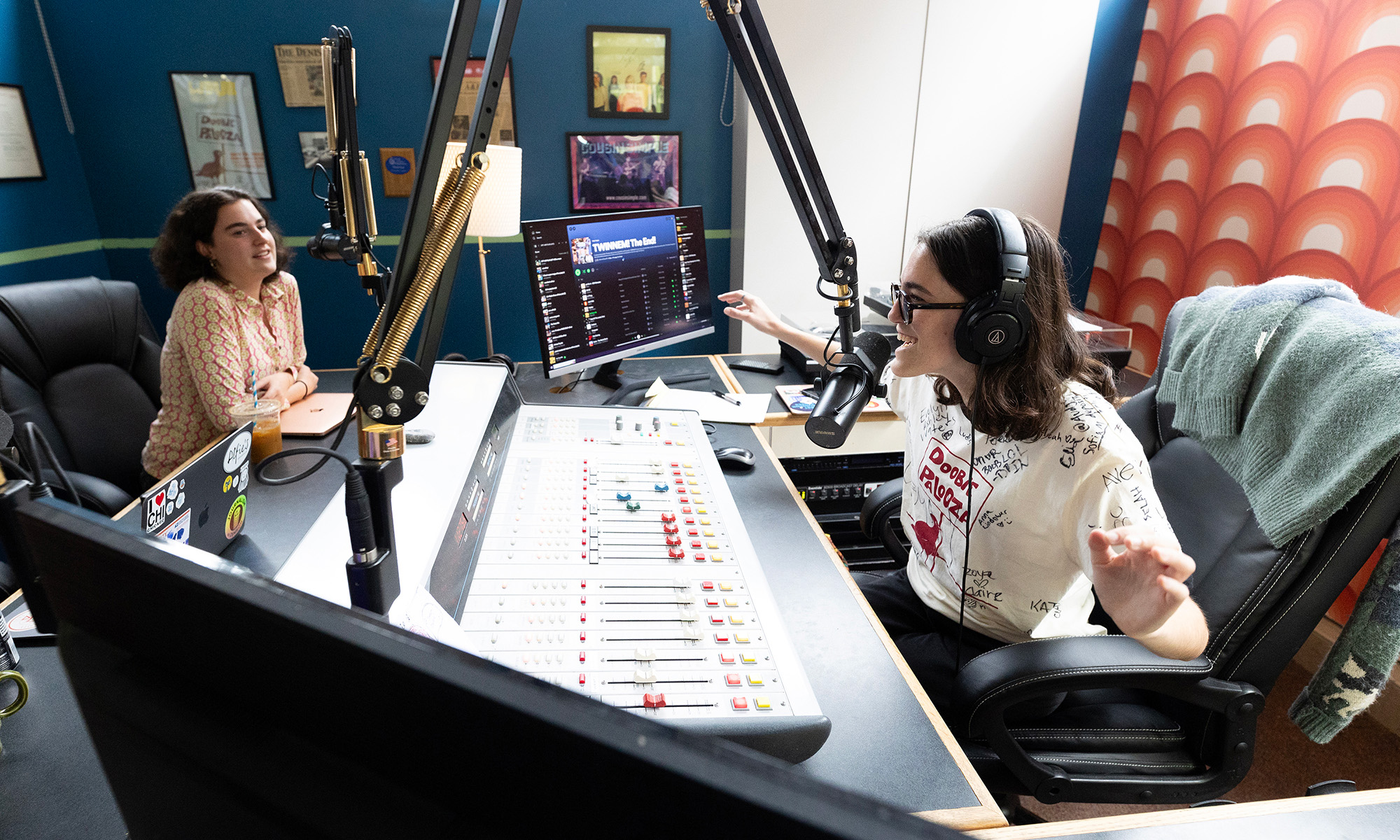 Two women sit across from each other in a radio broadcasting booth.