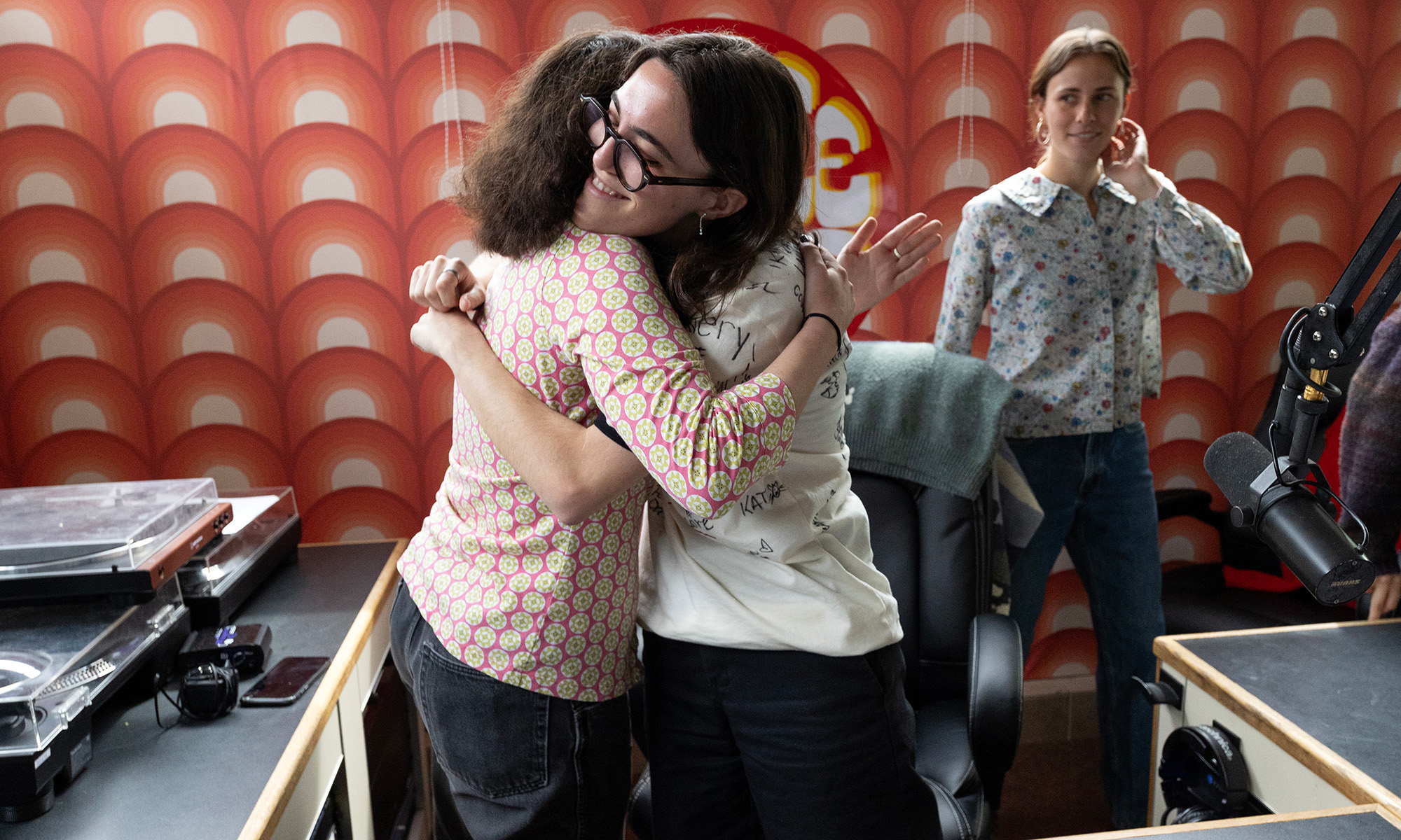 Two sisters hugging inside a radio broadcasting booth.