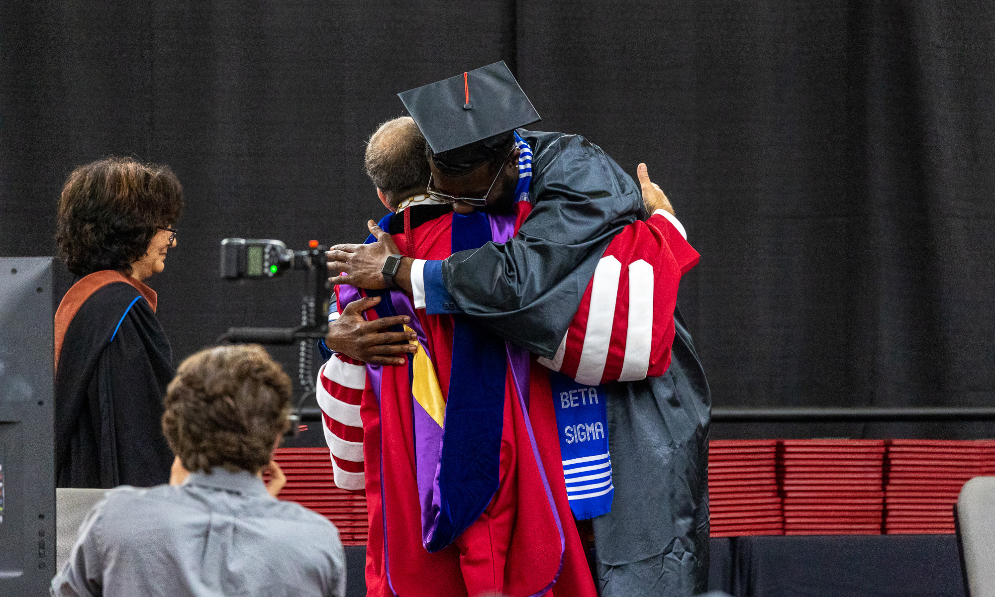 A student in a graduation robe hugging Denison President Adam Weinberg.