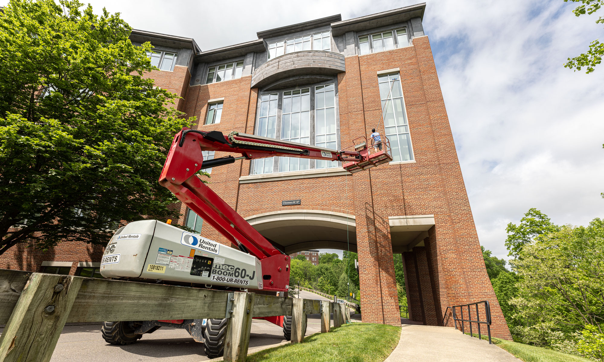 A man on a lift washing outside windows of a tall brick building. 