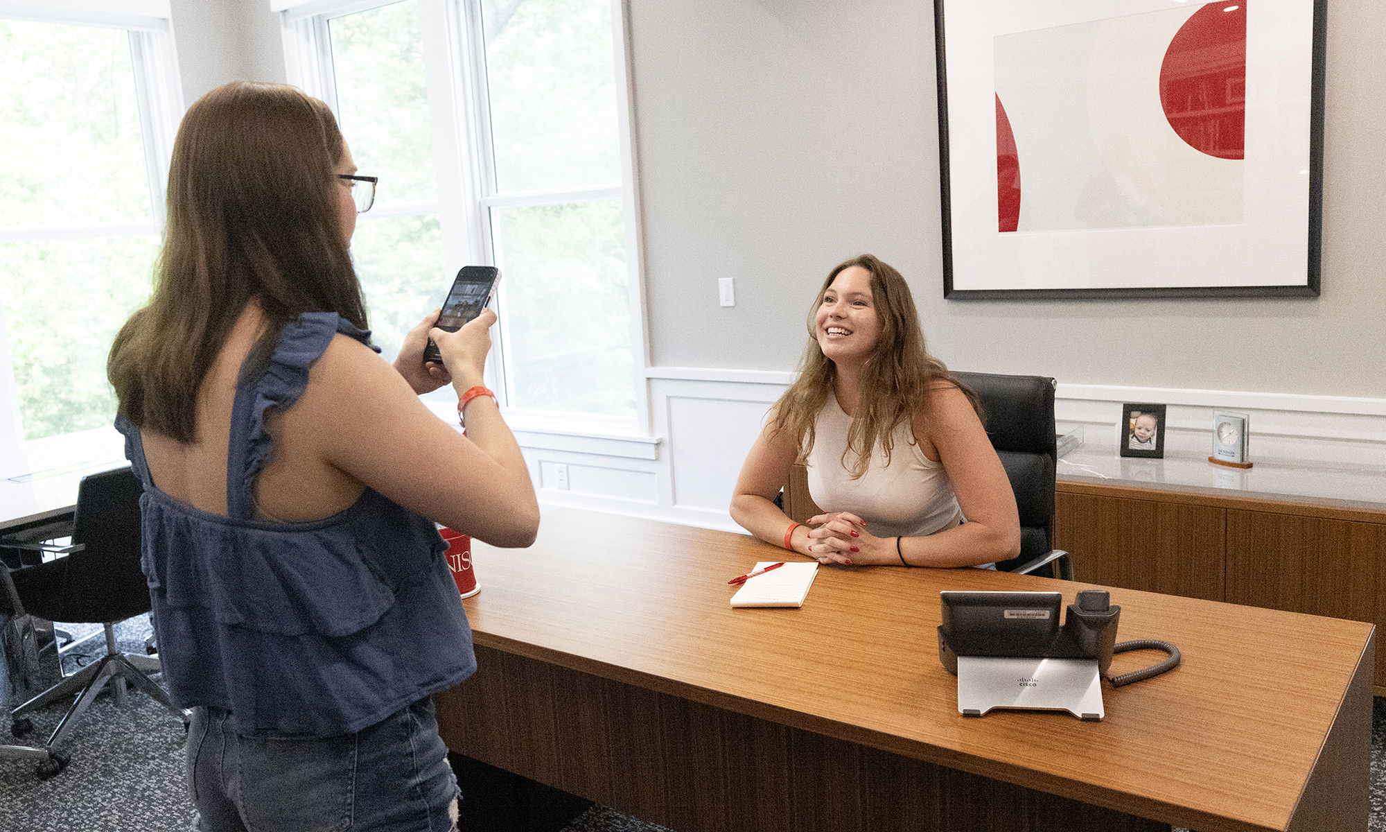 A student smiles for a photo behind the President's desk.