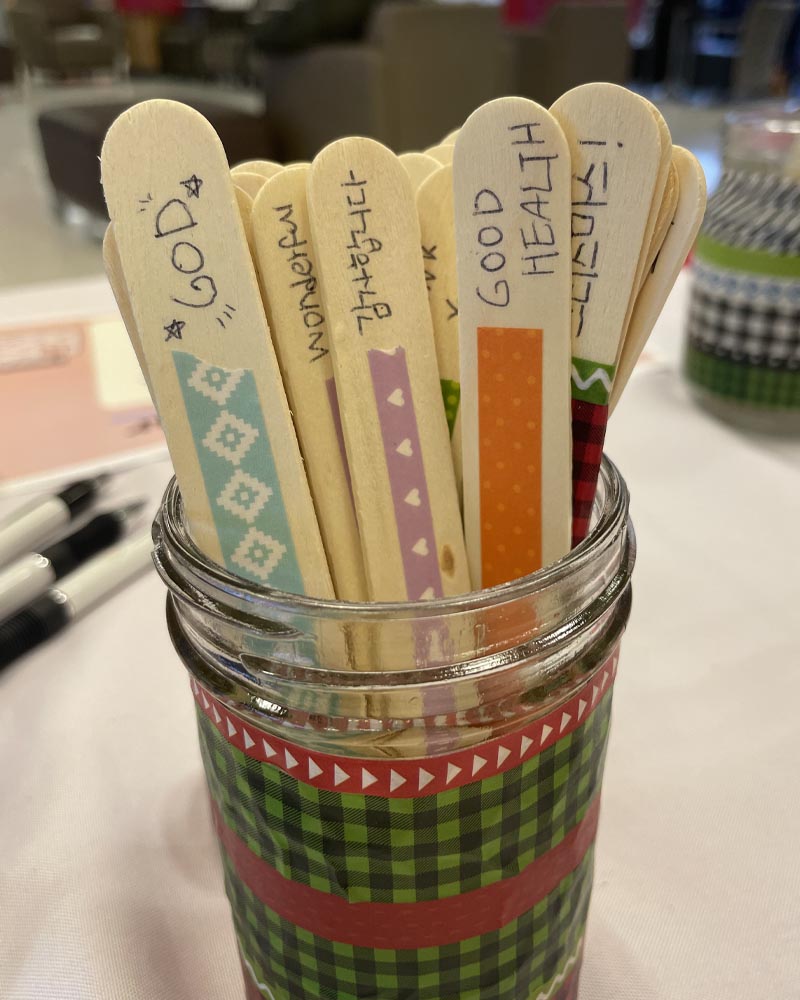 Glass jar with wooden popsicle sticks labels with phrases of gratitude.