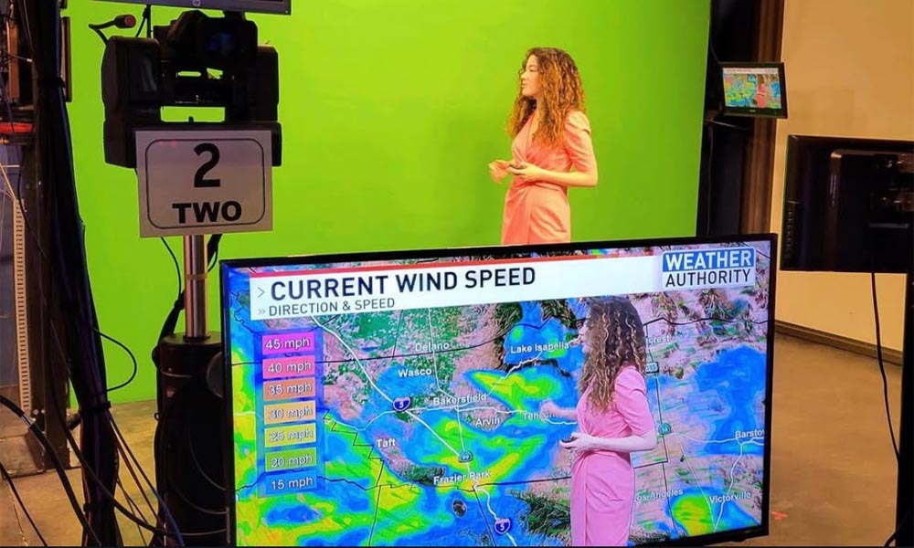 Lena Folke ’22 in a news studio delivering a weather report against a greenscreen; a television monitor sits in the foreground displaying the broadcast image of Lena in front of a weather map.