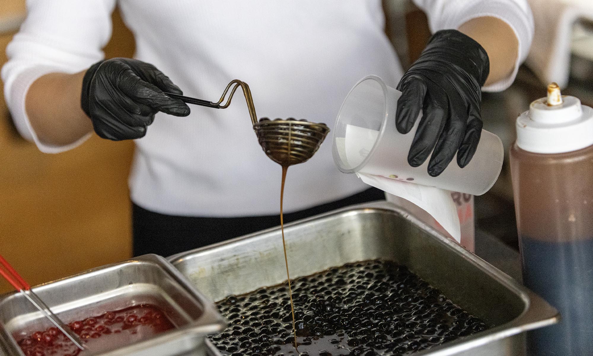 Photo: close up a Trucha employee wearing black gloves holding a metal scooper, scooping tapioca balls into a cup.